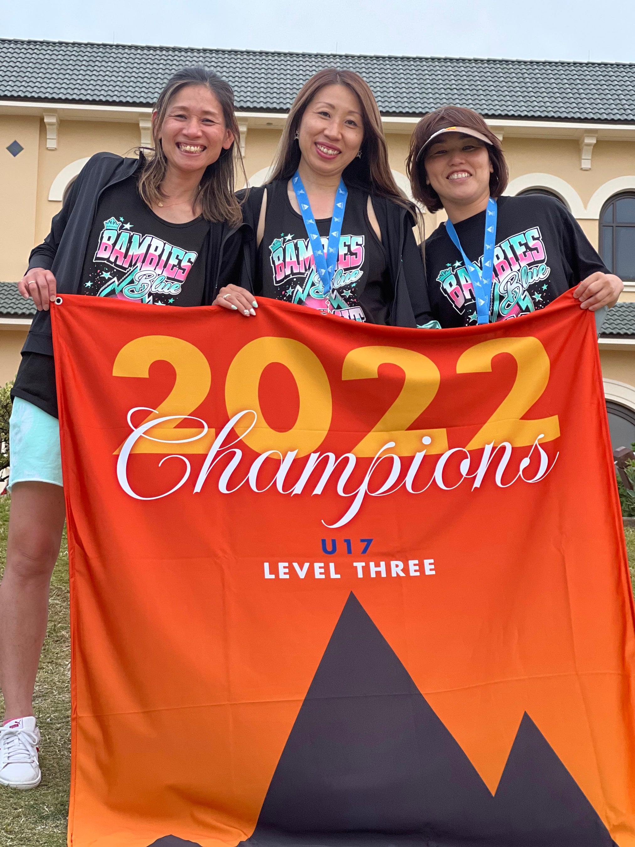 チャンピオンフラッグを持つコーチ陣（写真中央代表小田香）©Kawasaki Kids Cheerleadingclub BAMBIES All rights reserved