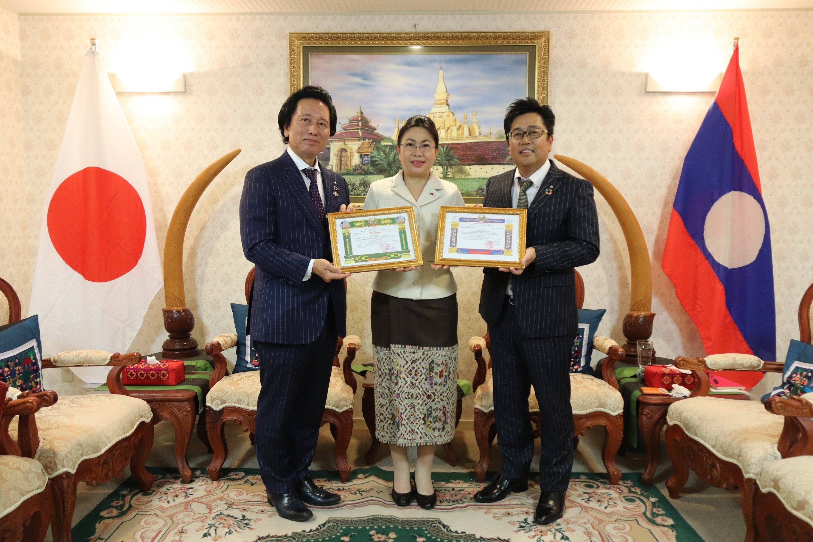 同国政府より感謝状を受け取る当社社長の津村佳宏（写真左）とフォンサムット・アンラワン特命全権大使（写真中央）、アデランス・ラオス社会長の千藤伸一（写真右）