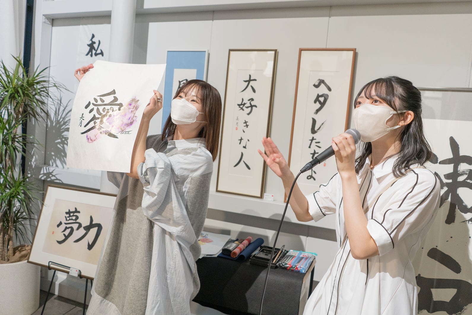 完成した作品「愛」を来場者に掲げる山内あいなと作品説明をする今村美月
