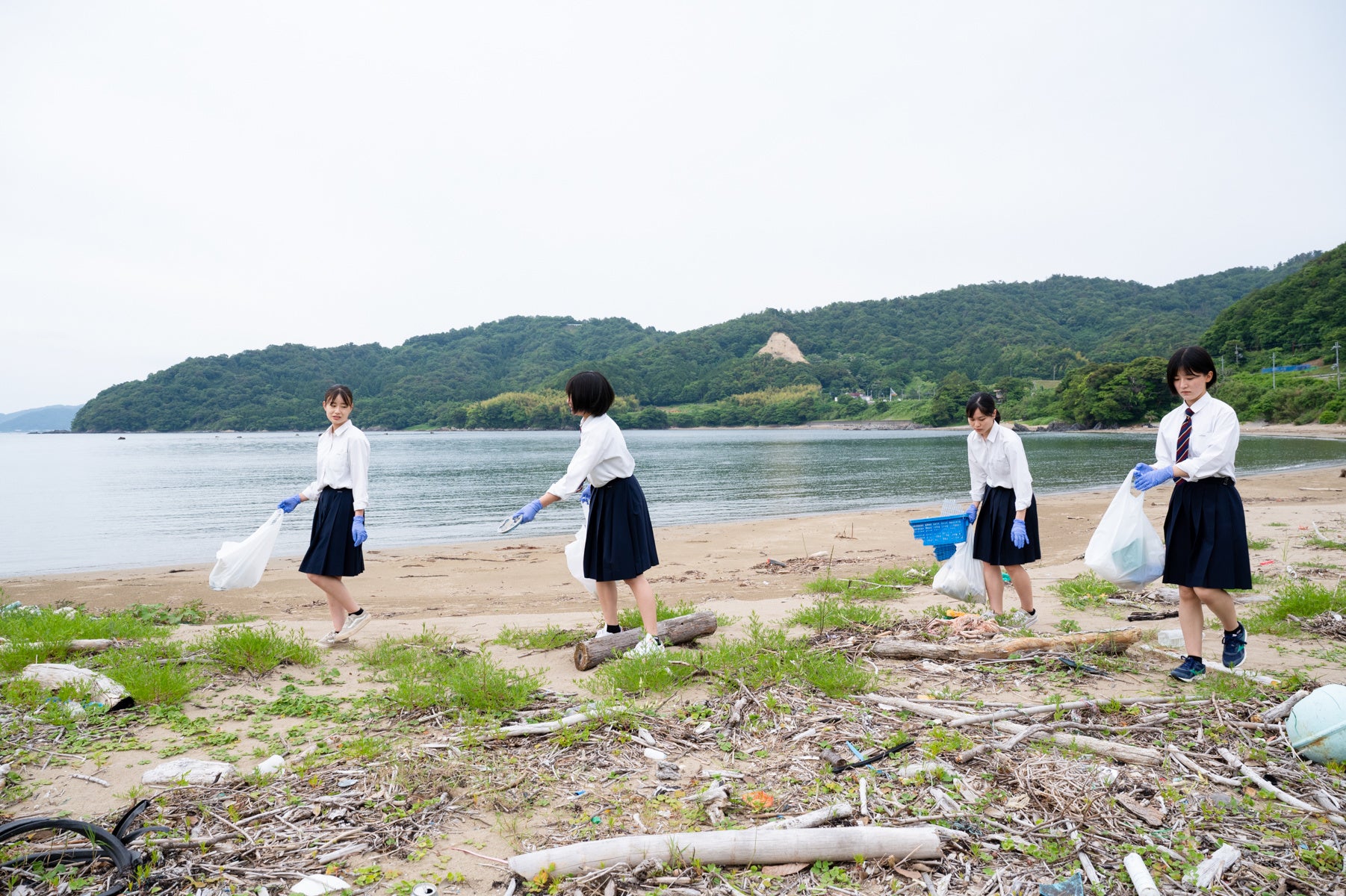 海辺でゴミ拾いをする女子高生たち