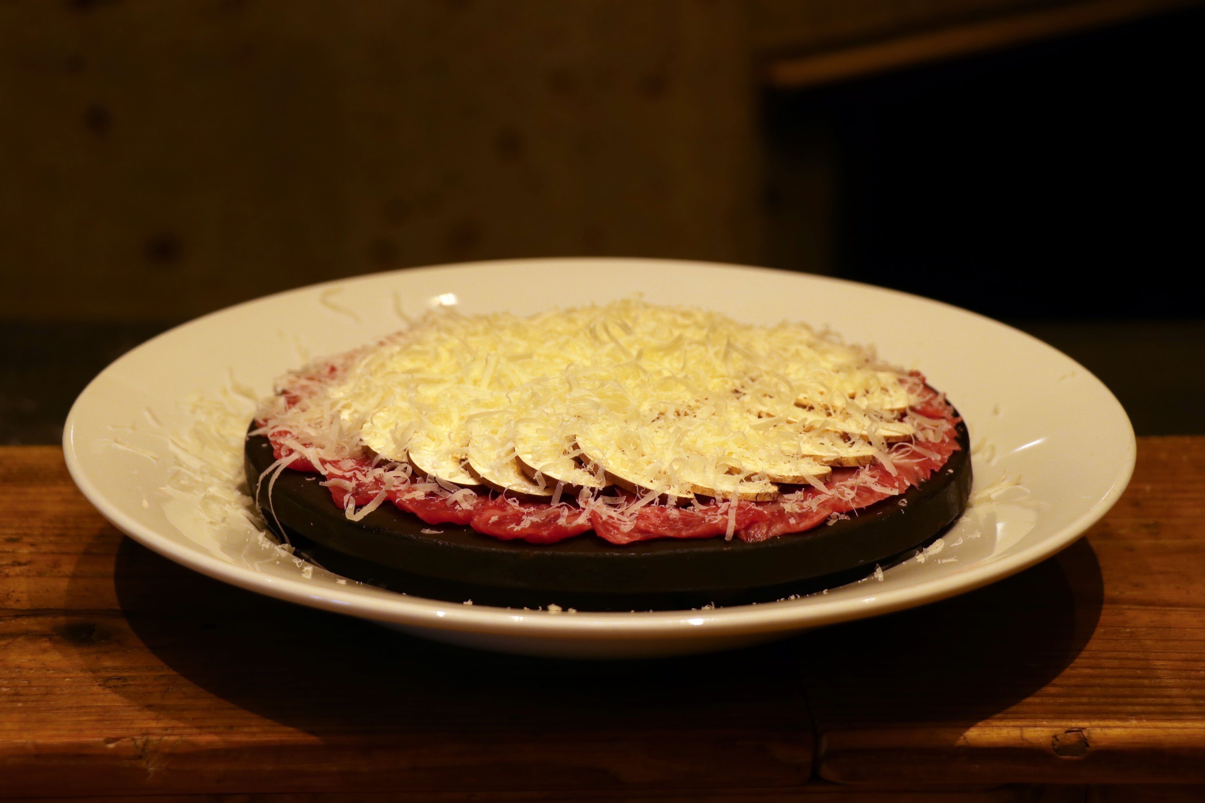 白い牛カルパッチョ：濃厚な味わいのパルメジャーノチーズをお客様の目の前ですりおろす、黒毛和牛の生肉とマッシュルームのカルパッチョ。