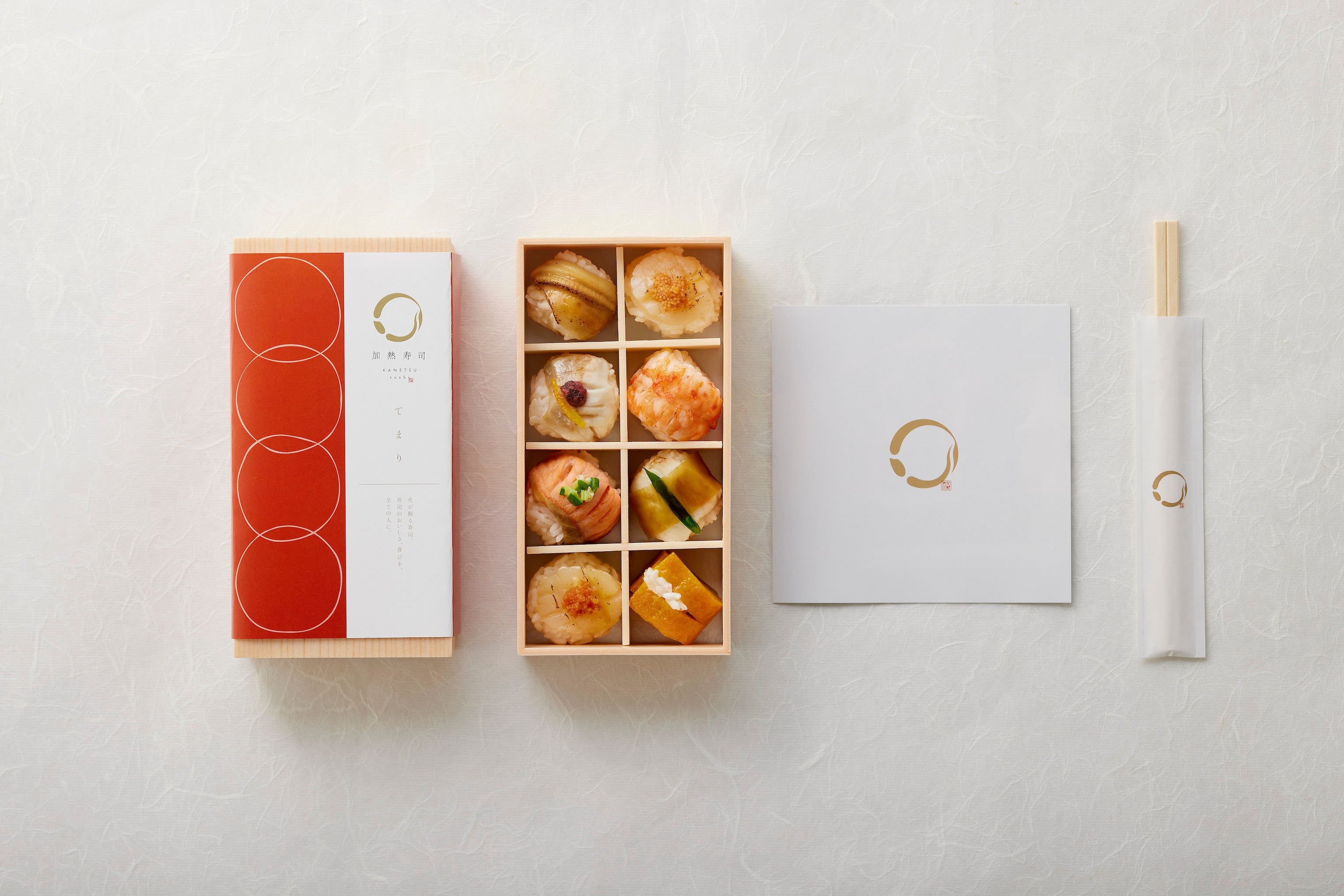 てまり寿司オリジナルの帯に包まれた木目調のトレーに入れて、パンフレットとお箸と一緒にお届けします。