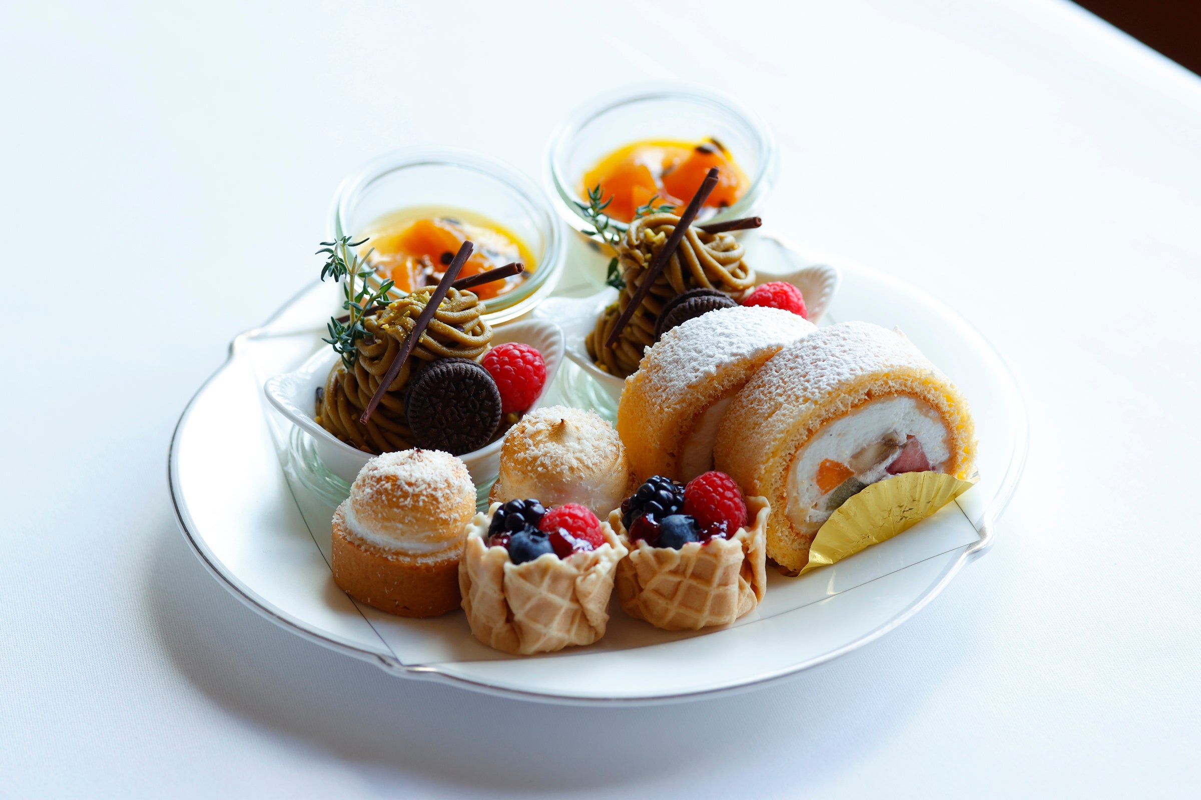 上段（奥から時計回り）：ベイクドレアチーズ  アプリコットとパッションフルーツソース、ピスタチオのモンブラン、ミニフルーツロール、バスケットルージュ、ライムとココナッツのミニタルト