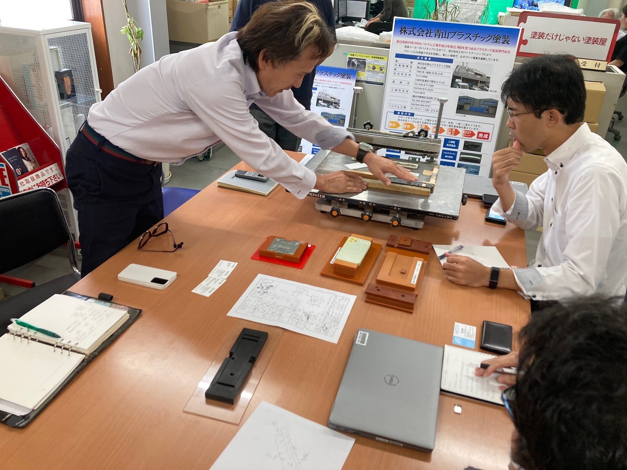 治具の説明をする青山社長（写真左） 株式会社青山プラスチック塗装