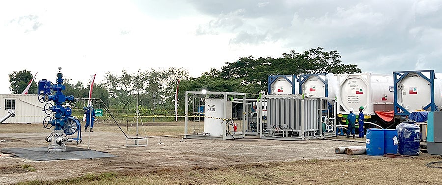 インドネシア・西ジャワ州の陸上ジャティバラン油田におけるCO2圧入サイト。 写真右側の白いタンクからCO2を 供給し写真左側の坑井（青い構造物）からCO2を圧入する。