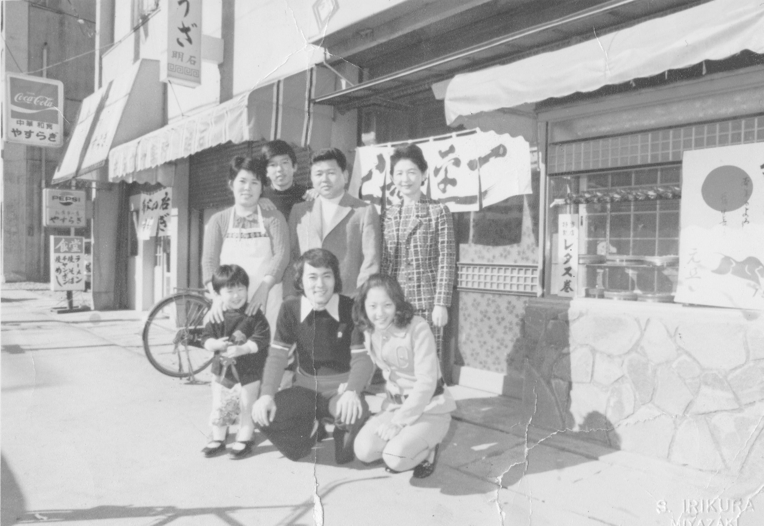 先代社長（後列中央）と平尾昌晃氏（前列中央）一平寿し店先にて（昭和四十年代撮影）