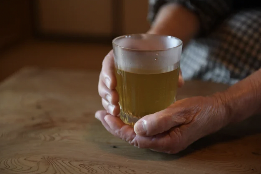 画像の説明：あたたかいお茶の入ったグラスを両手に持った様子