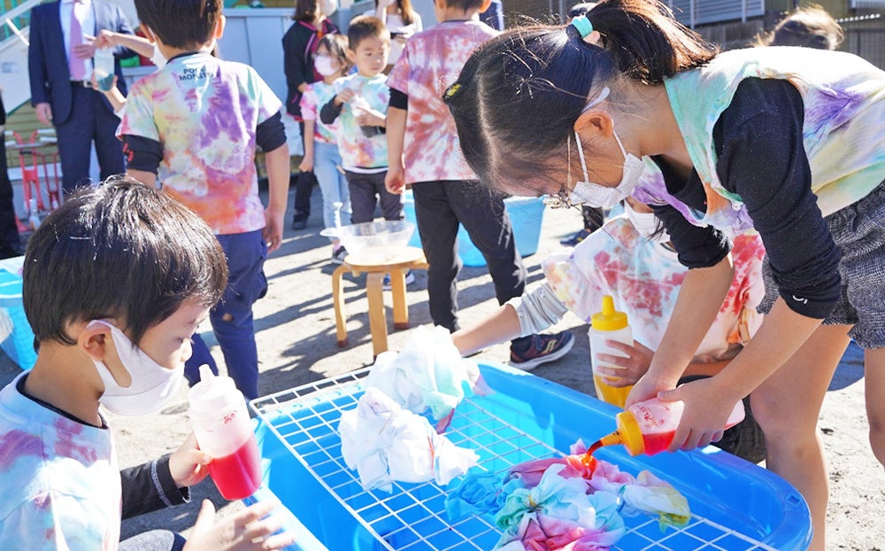 （晴天に恵まれ、園庭に染色道具を広げてにぎやかに、真剣に染めていく）