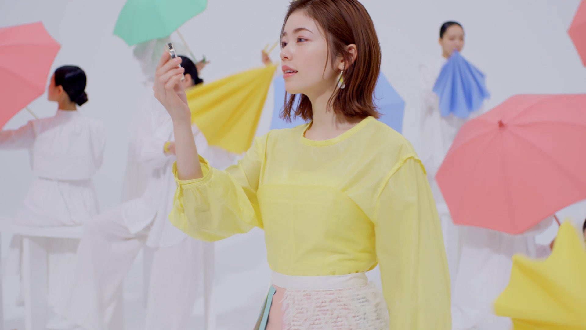 1.「マシュマロフィニッシュパウダー ~Abloom~」を手に持った小芝さんの後ろで、女性たちが次々とカラフルな傘を開いていきます。