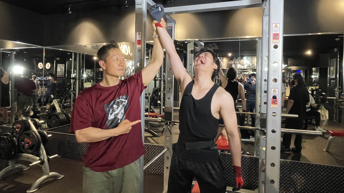 ©TVO ベンチプレス100㎏を達成した前田拓哉アナウンサーの腕を掲げて称える谷本道哉先生 2022年6月3日撮影