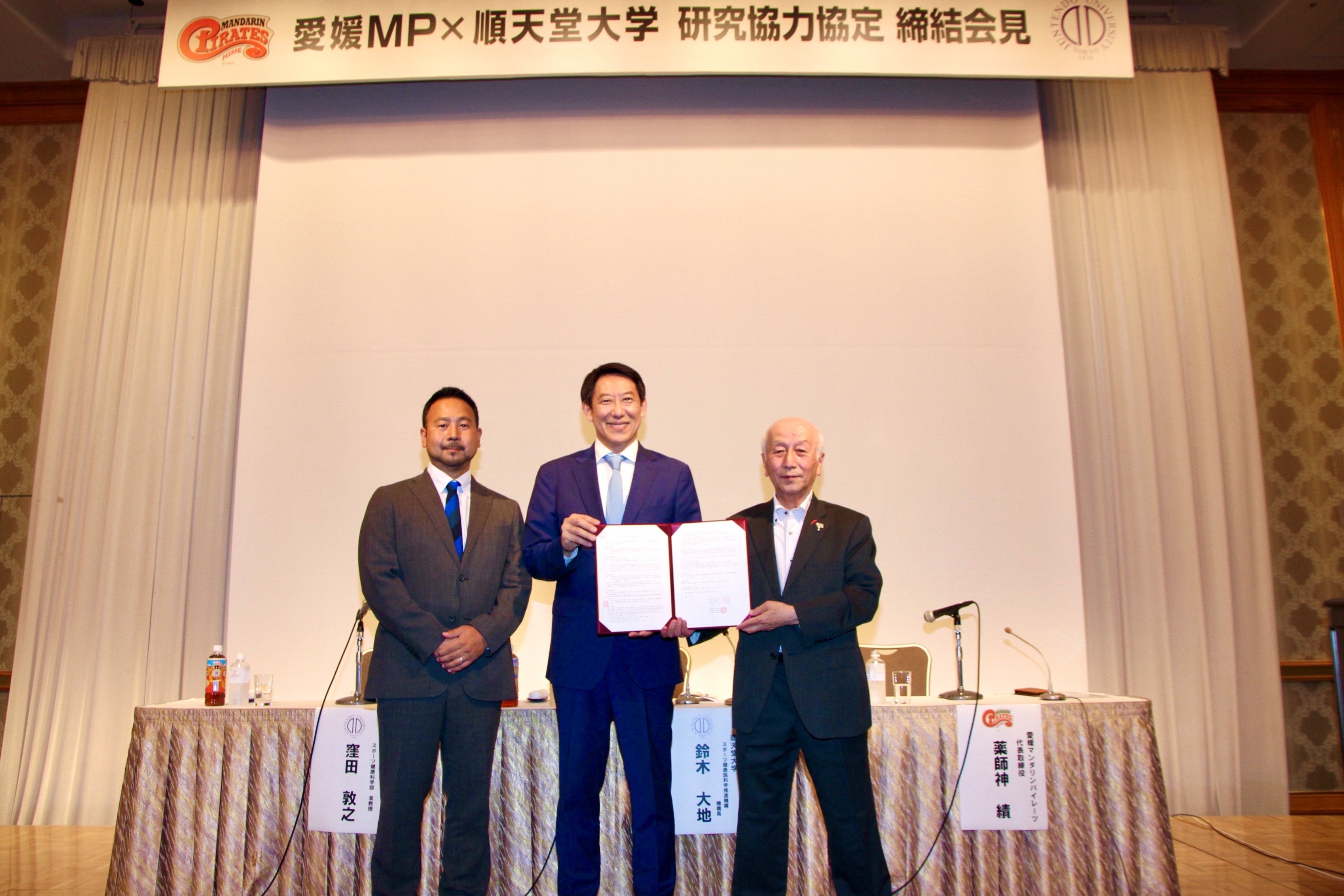 協定書を持って写真撮影に応じる登壇者（左から順天堂大学：窪田敦之准教授、鈴木大地機構長、愛媛県民球団株式会社：薬師神績代表取締役）