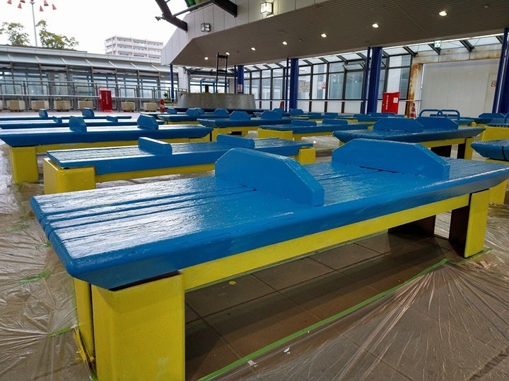 太陽の降り注ぐ半屋外の広場に、黄色と青色が映えるベンチが完成しました