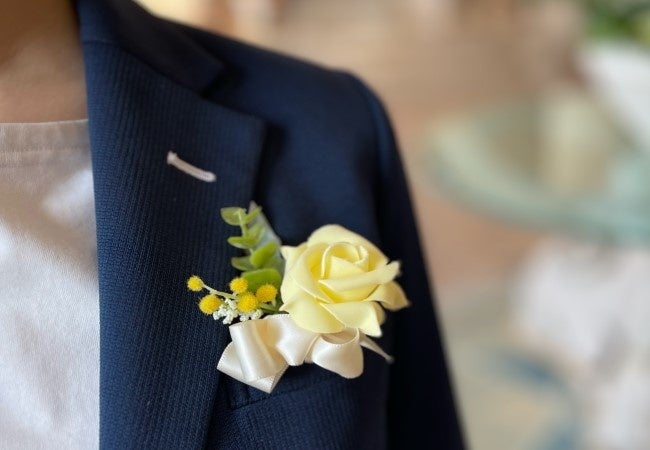 期間中は、手作りのハッピーイエローコサージュを身につけて お客様をお迎えいたします。