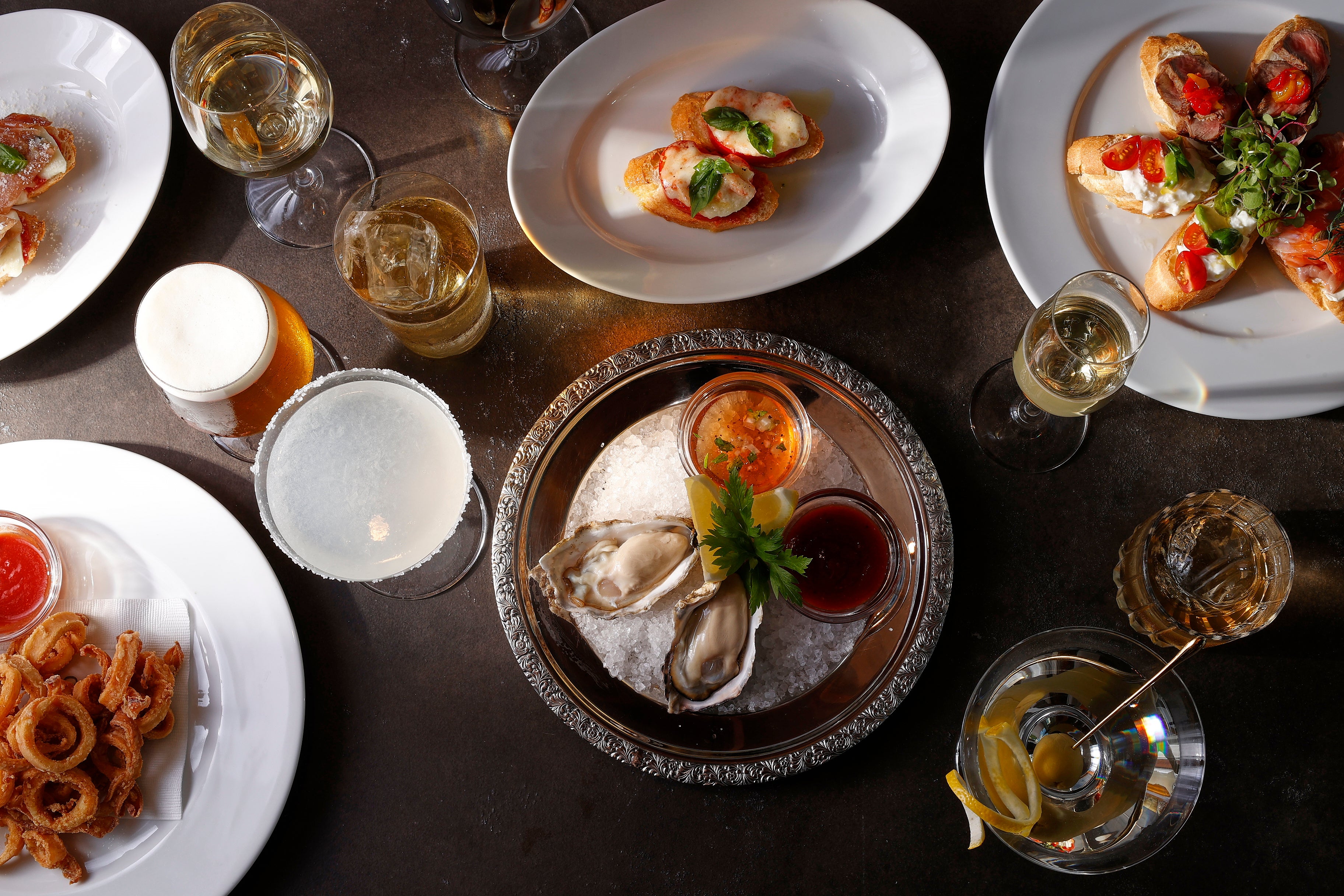 ＜ハッピーアワーご提供フードの一部　右上から時計回りに　 3種のクロスティーニプレート、フレッシュオイスター2ピース、ヤリイカのフリット、ハムとチーズのクロスティーニ、モッツァレラチーズ＆トマトクロスティーニ＞