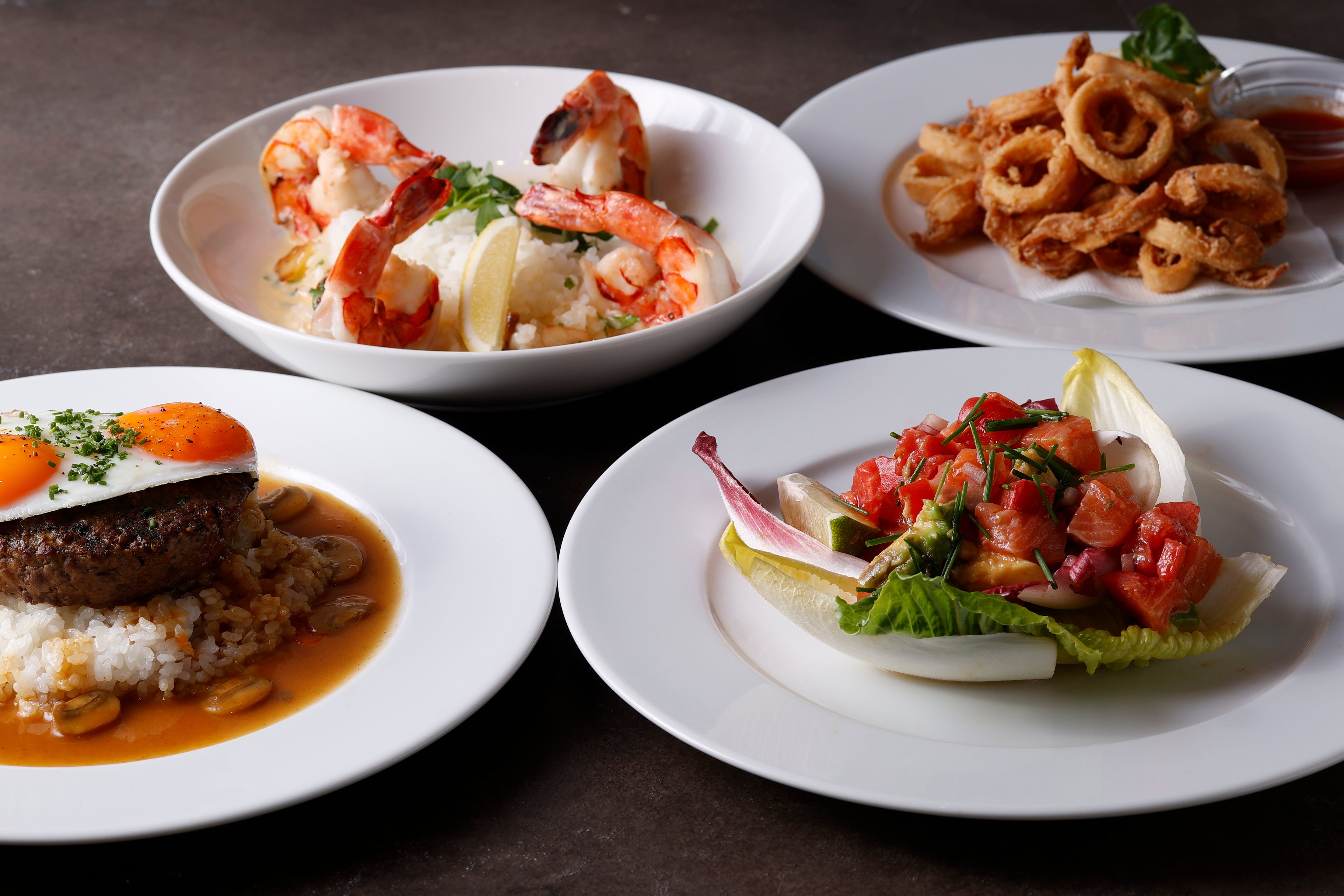 ＜バーバイトメニューの一部　左上から時計回りに　ガーリックシュリンプ、ヤリイカのフリット、サーモンとアボカドのサラダ、ロコモコ＞