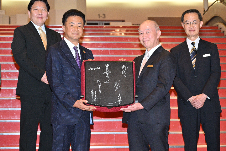 株式会社中野サンプラザ代表取締役会長 金野 晃様から、 当社 代表取締役社長 松尾 大作への、記念の椅子贈呈の様子