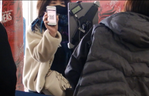 スマホに表示のQRコードと 入場者自身の顔をiPadにかざす様子