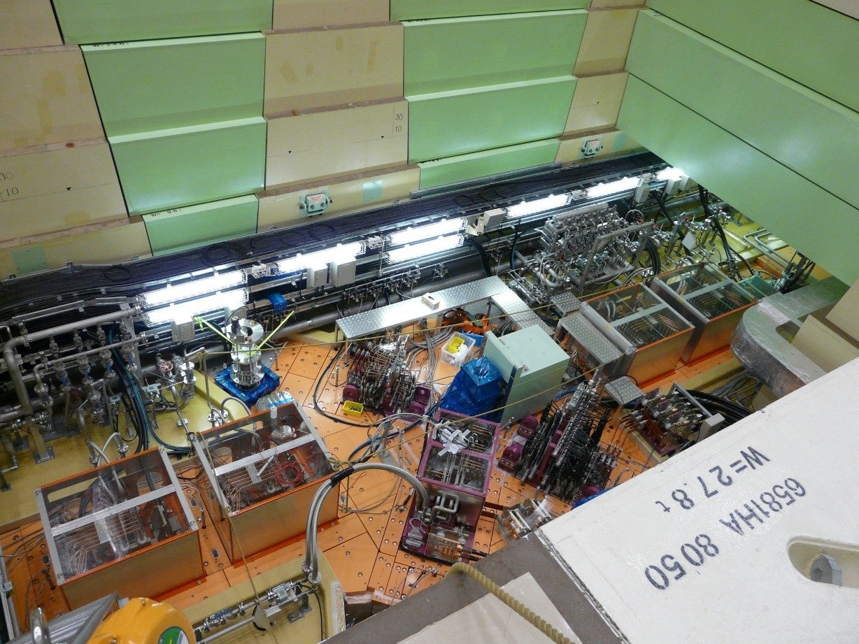 ミュオン生成エリア：保守エリアの床面（橙色）から2.4 m低いビームラインにミュオン回転標的を設置。左下から右上に向かう陽子ビームの経路上に設置されたミュオン回転標的でミュオンが生成。四方向（写真撮影時は三方向のみ）の紫色の電磁石で実験室に取り出される