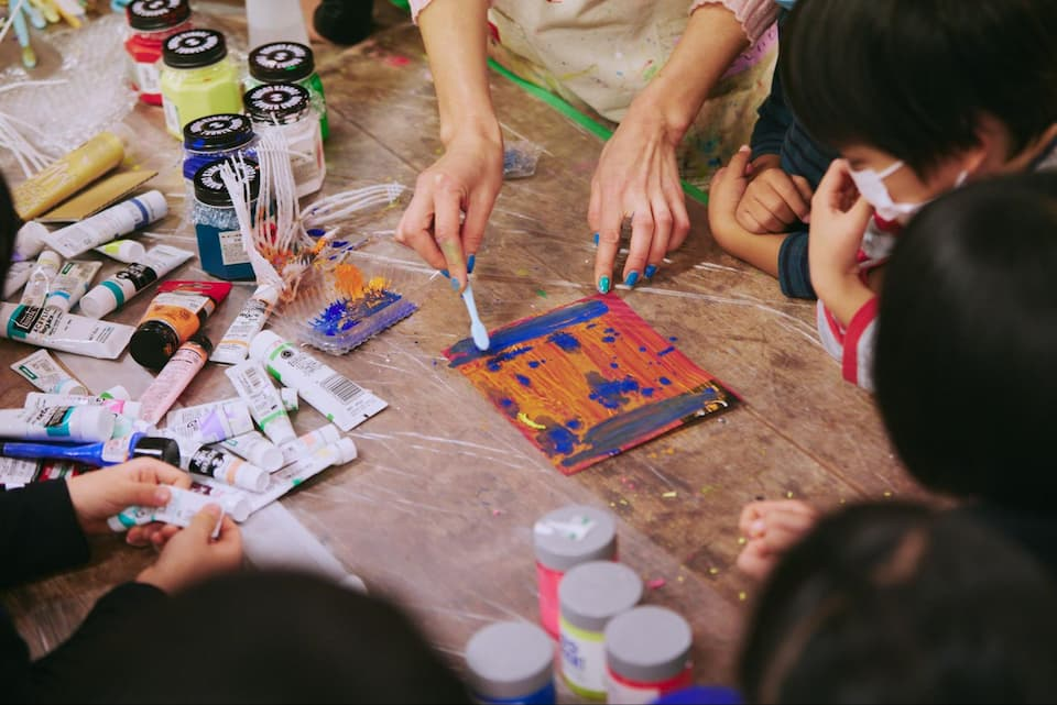 （段ボールやローラー・歯ブラシ・果物を包むフルーツキャップなどを使って色を塗っていく様子）