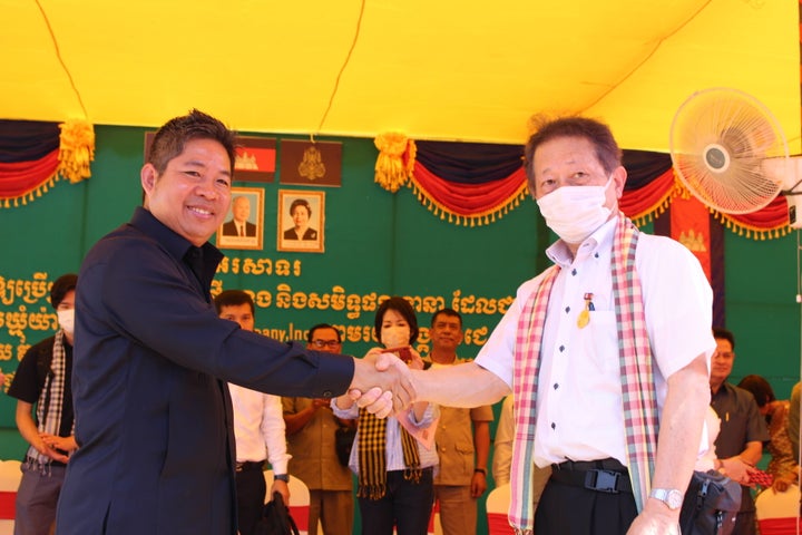寄贈式で、カンボジア王国司法省秘書官のカエット シカノ氏（左）と握手をする当社取締役・柴田（右）
