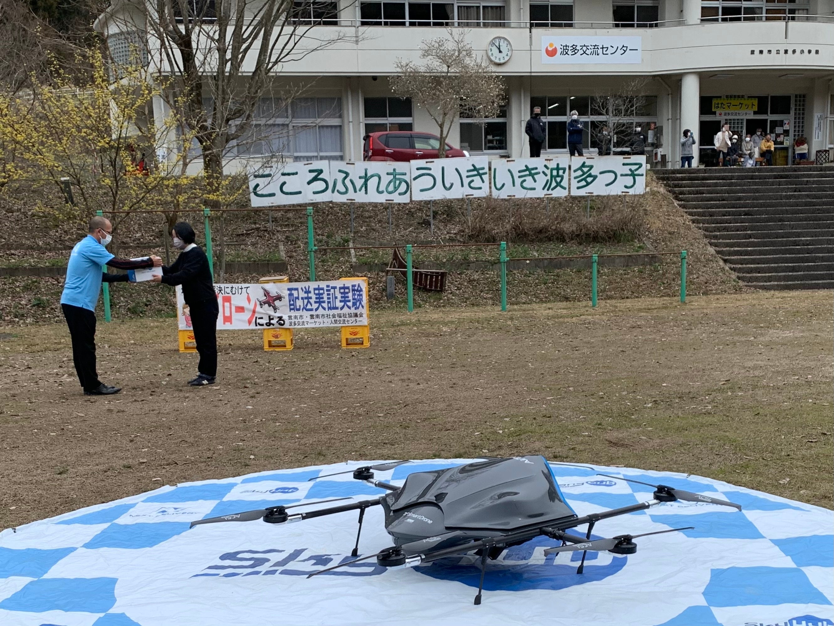 おでんと焼鯖弁当の入ったドローン用の箱を受け取るスタッフ