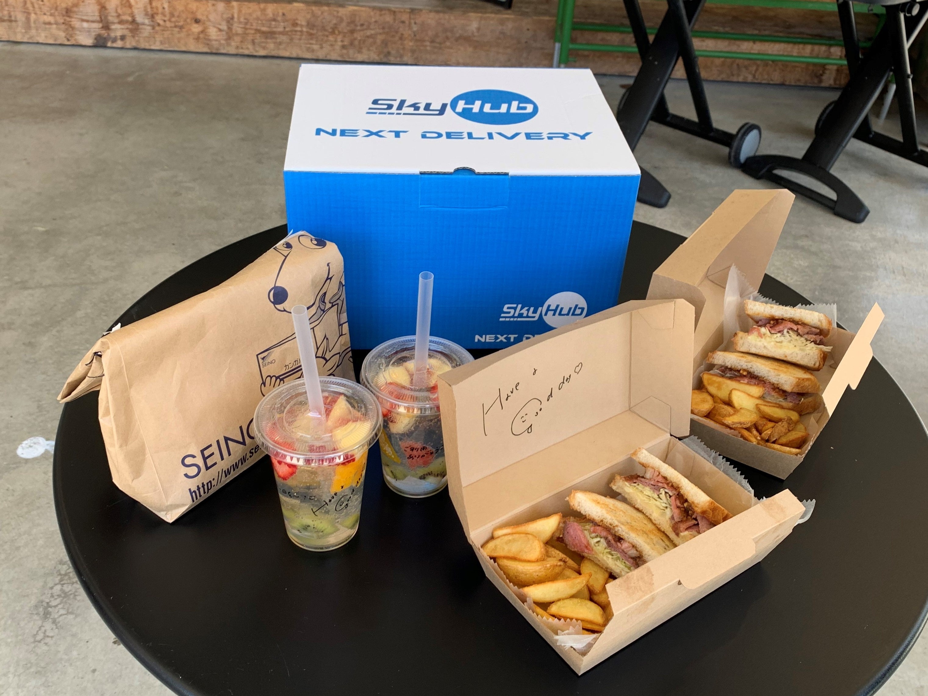 ドローン配送された共同配送の荷物と隼Lab.内Sanのサンドイッチとドリンク