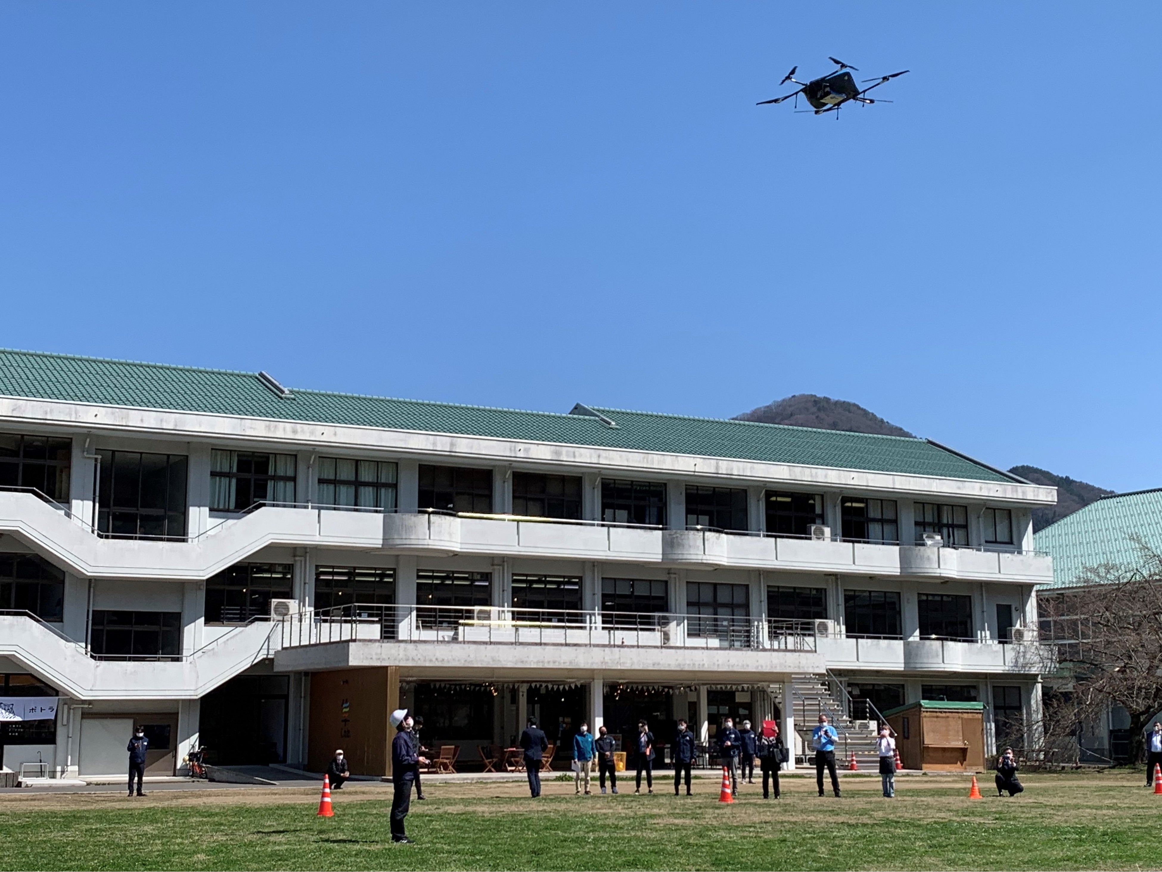 共同配送の荷物と隼Lab.内Sanのサンドイッチとドリンクを載せて離陸する物流専用ドローン”AirTruck” （隼Lab.前グラウンド）