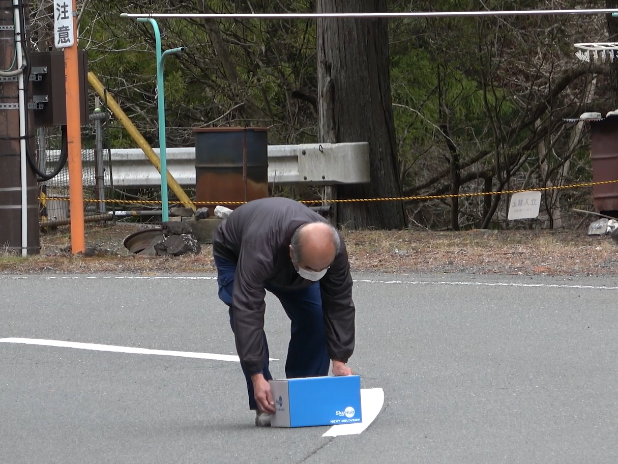 安全確認後、ドローン配送された荷物をピックアップする中津川区長 （崩落地点を超えた先の着陸地点）