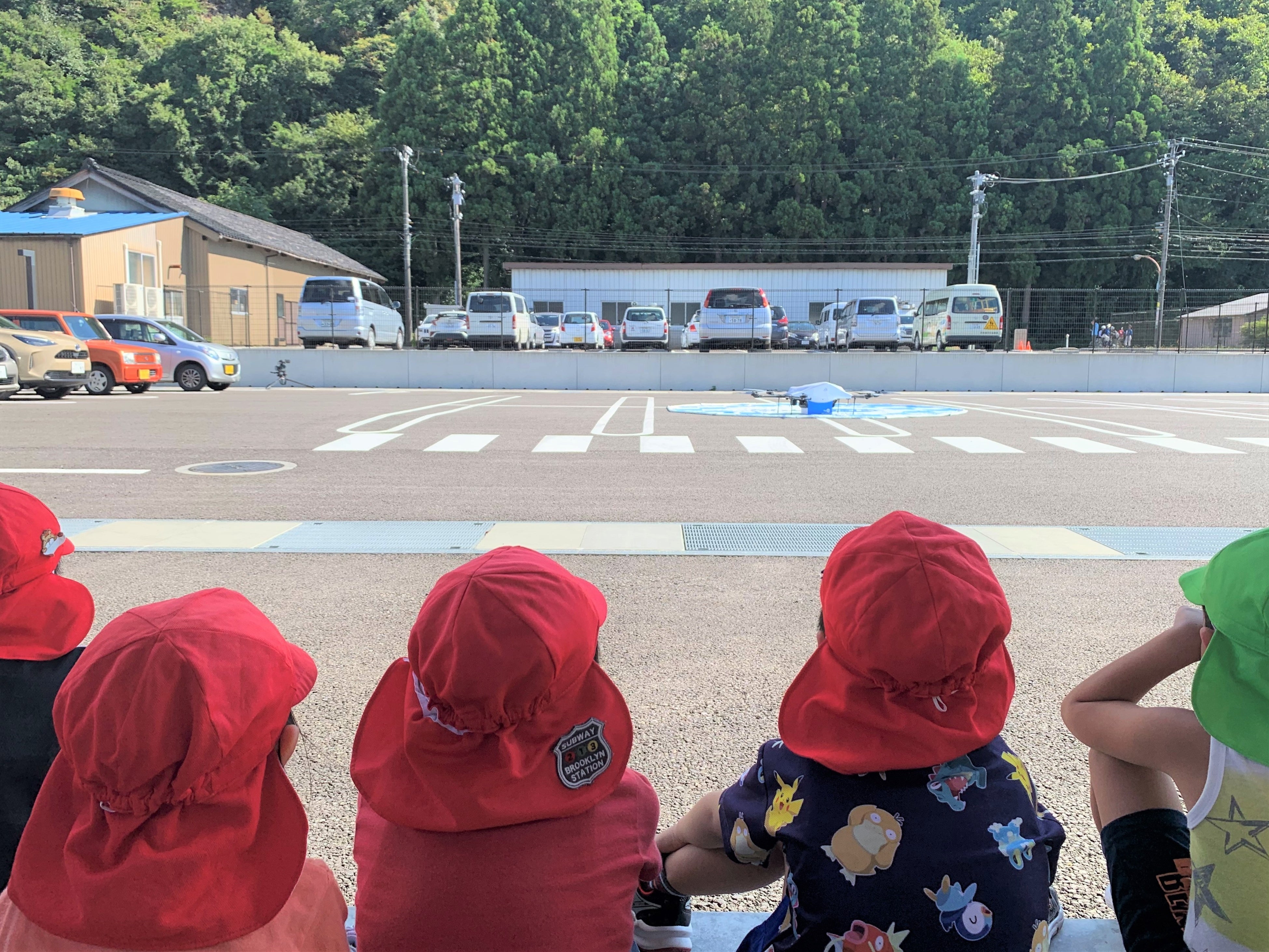お菓子を載せた物流専用ドローンAirTruckの着陸と荷物の切離しを見守る地元の園児達 （松東こども園）