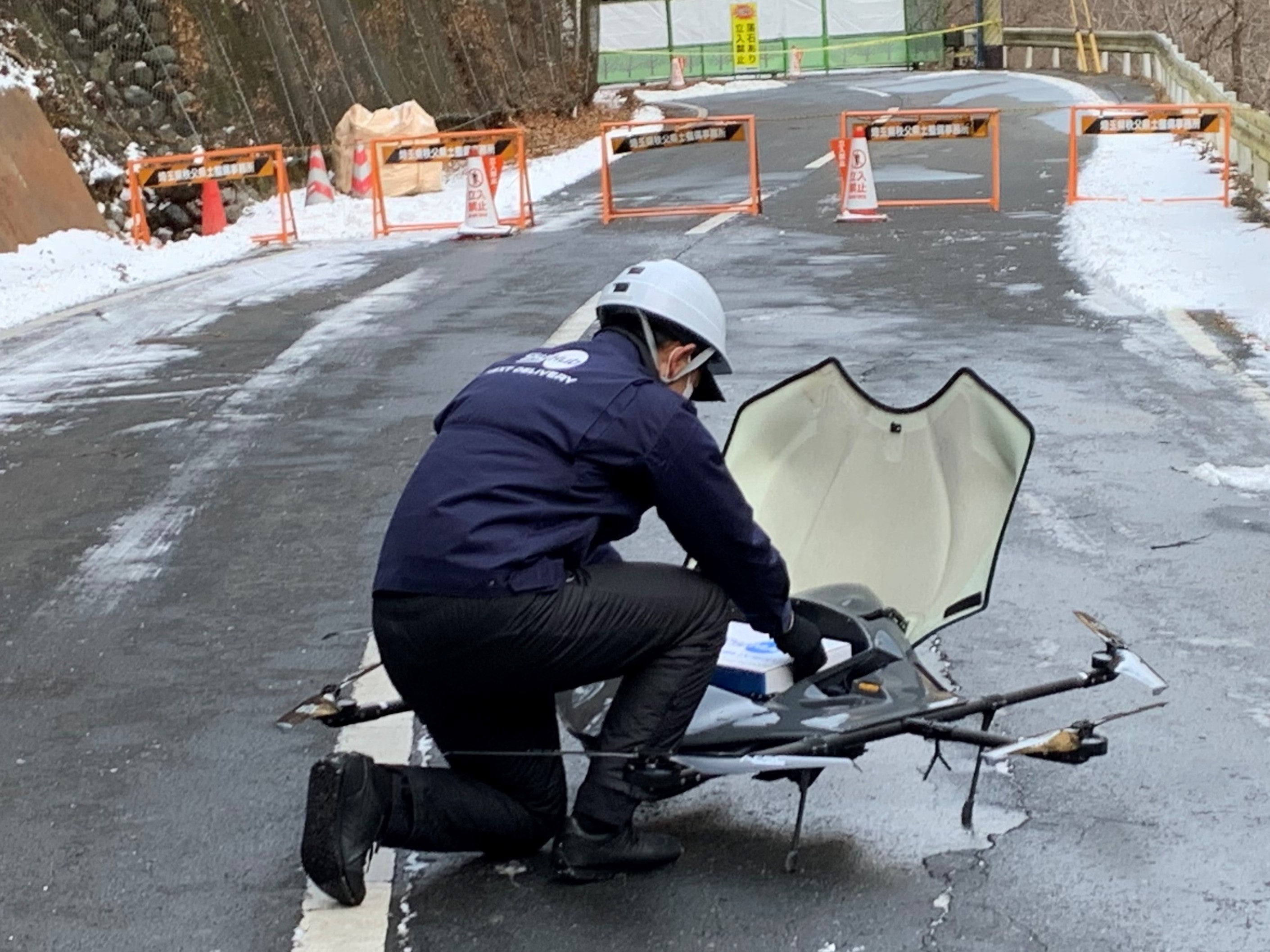 お弁当や新聞の入った箱をドローンに取り付けるスタッフ