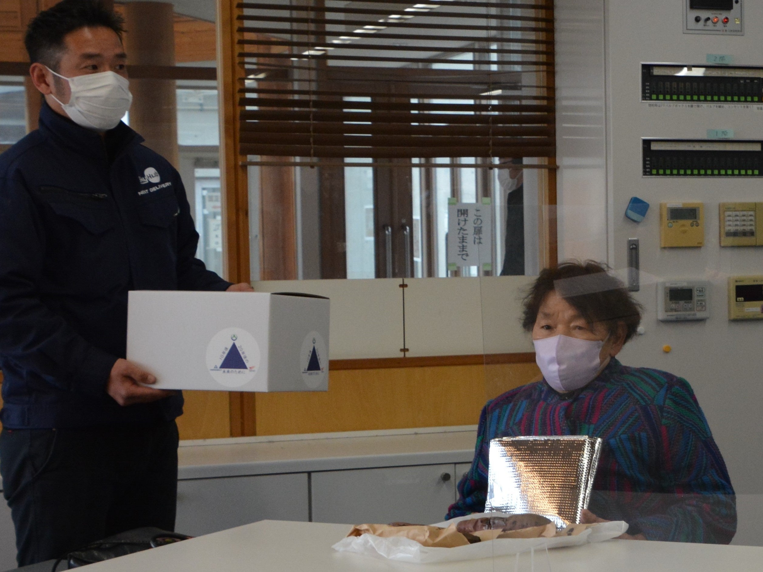 オンライン診療後ドローン配送で届いた処方薬と焼き芋を受け取る鈴木美智恵さん （仮ドローンデポ：旧九十九小学校）