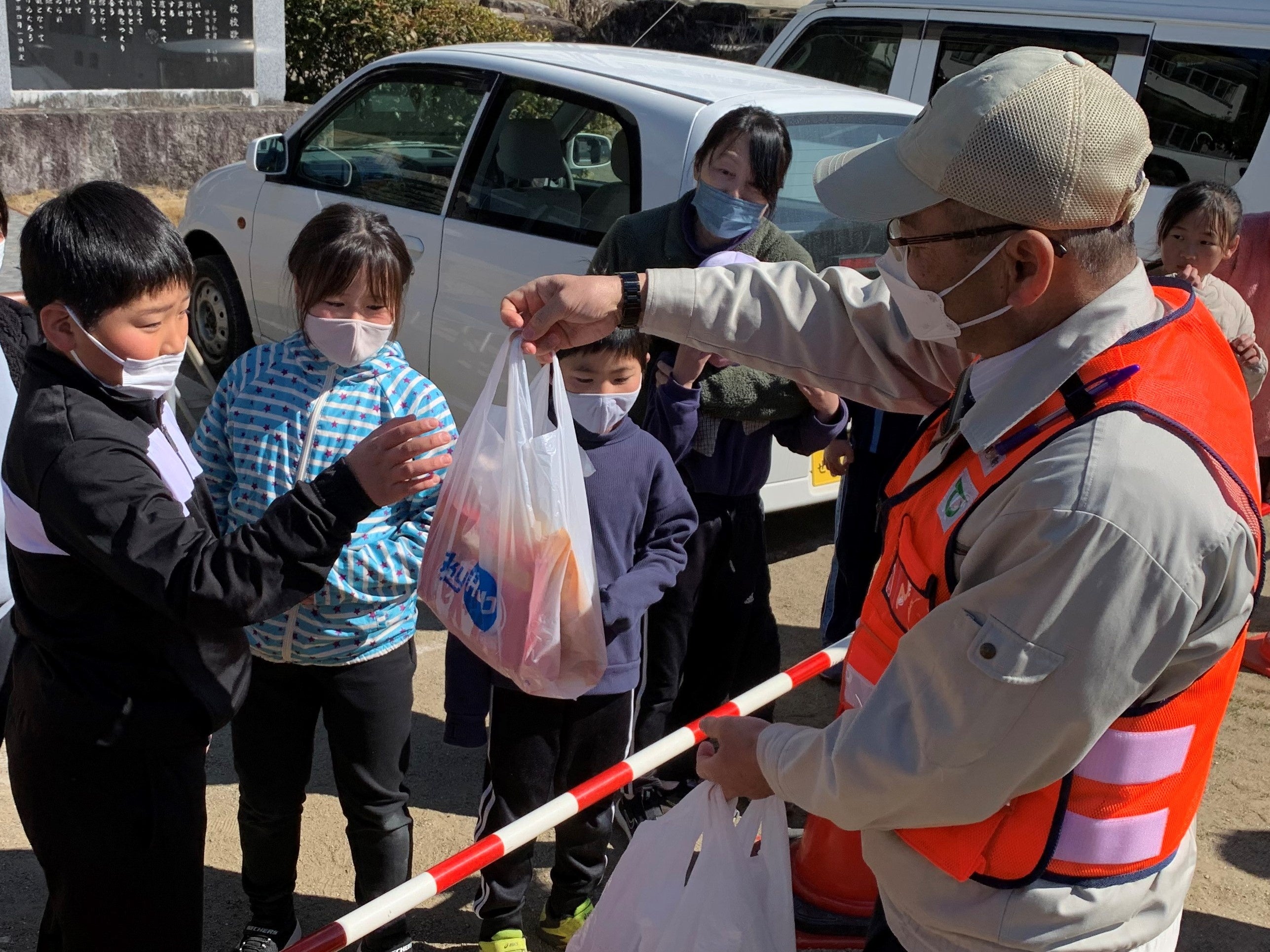 ドローン配送されたお菓子やカイロ等を永嶺天龍村長から受取る天龍村小学校の児童 （天龍村小学校グラウンド）