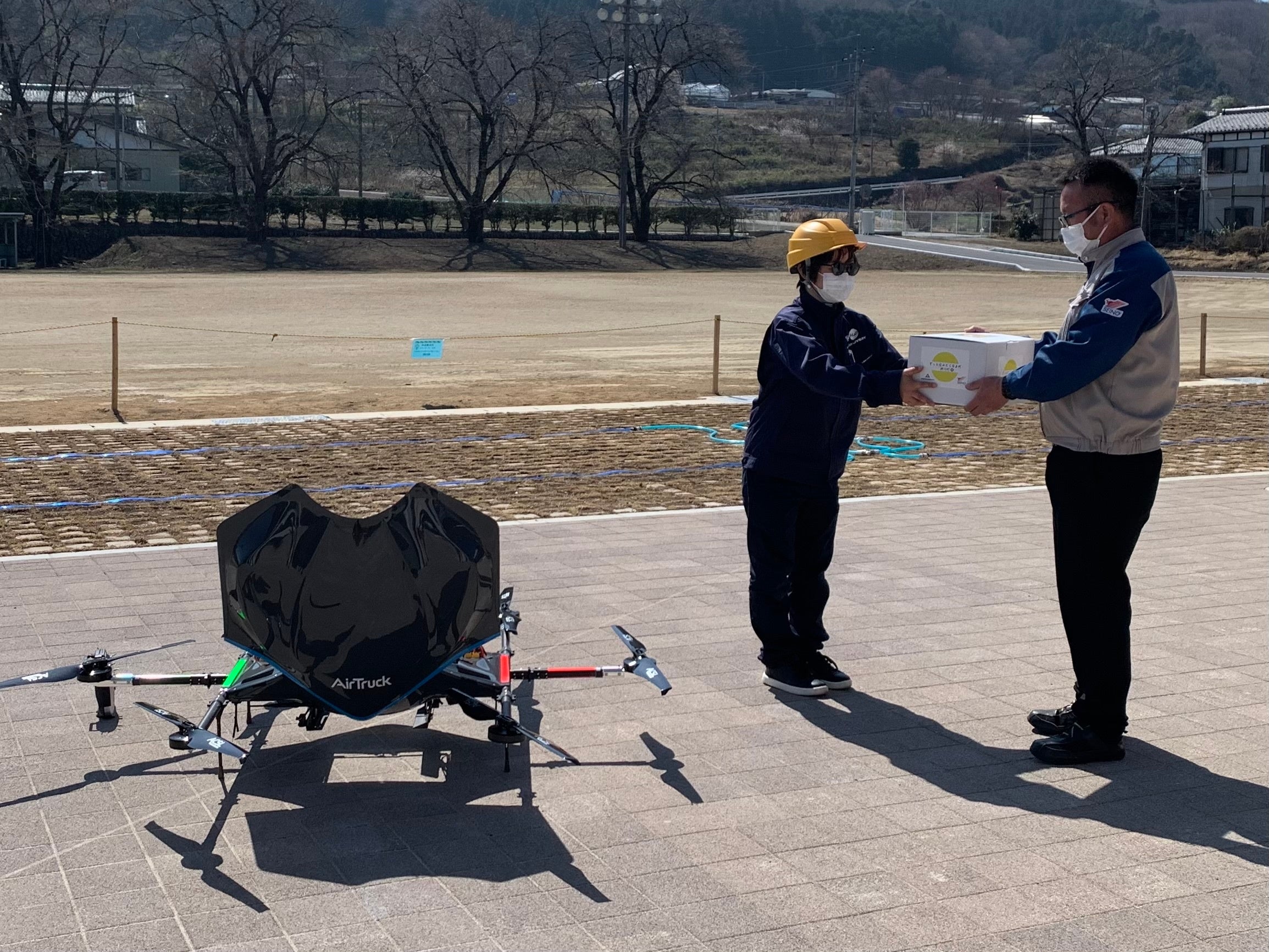 ドローン配送されたサイクリストのお土産が入った箱を陸送スタッフに手渡し （神川町多目的交流施設）