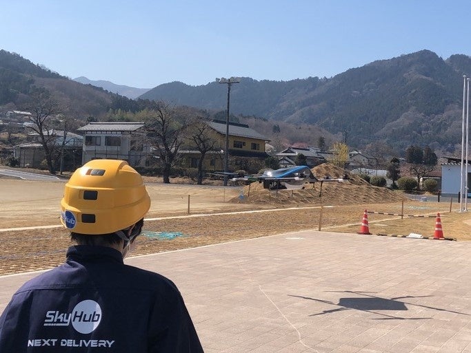 サイクリストのお土産を載せた復路飛行をするドローンの着陸を見守るスタッフ （神川町多目的交流施設）