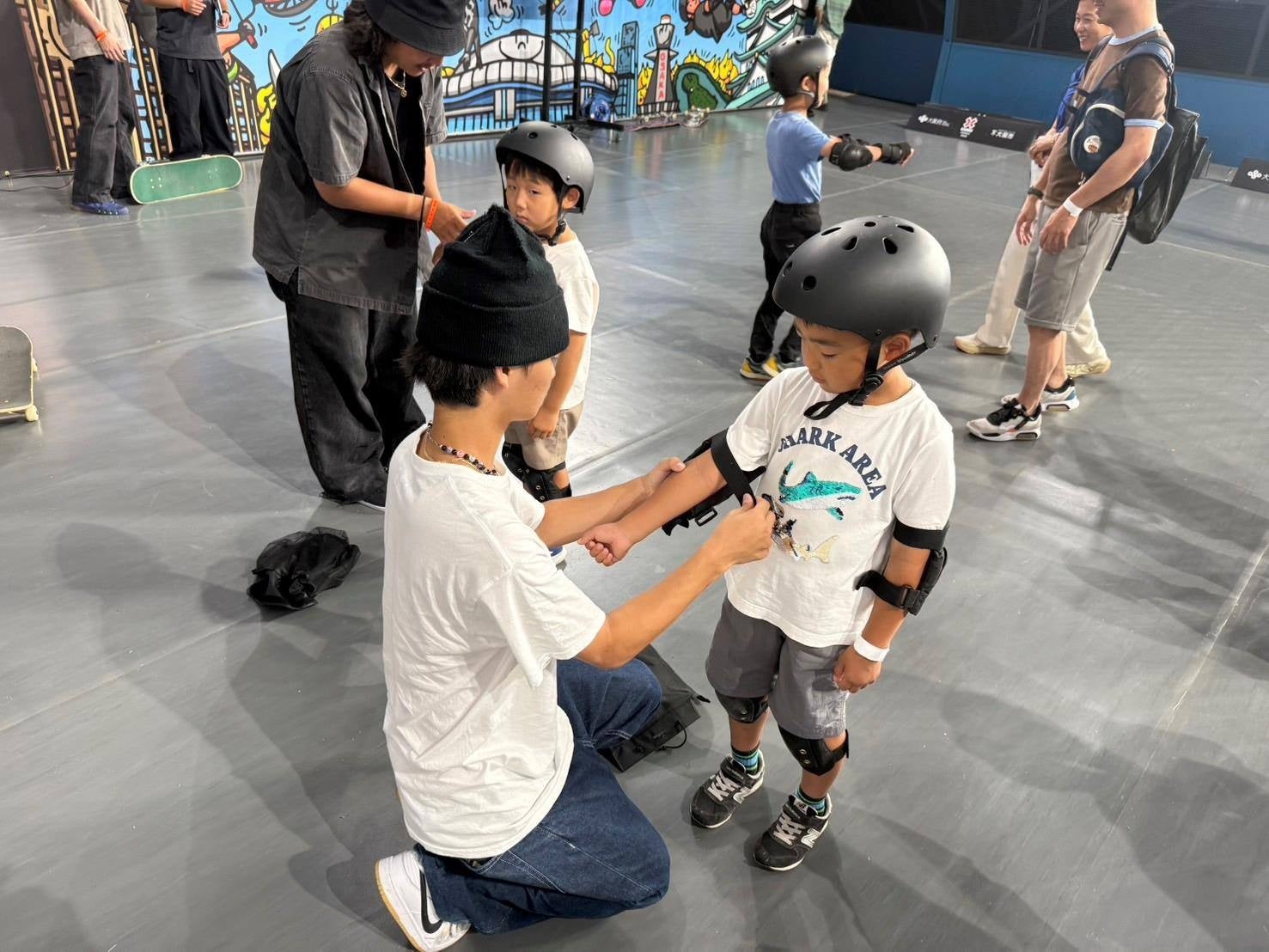 X Games Osaka 2025で実習として参加者にプロテクターを装着するJWSC国際スノーボード&スケートボード専門学校の学生達