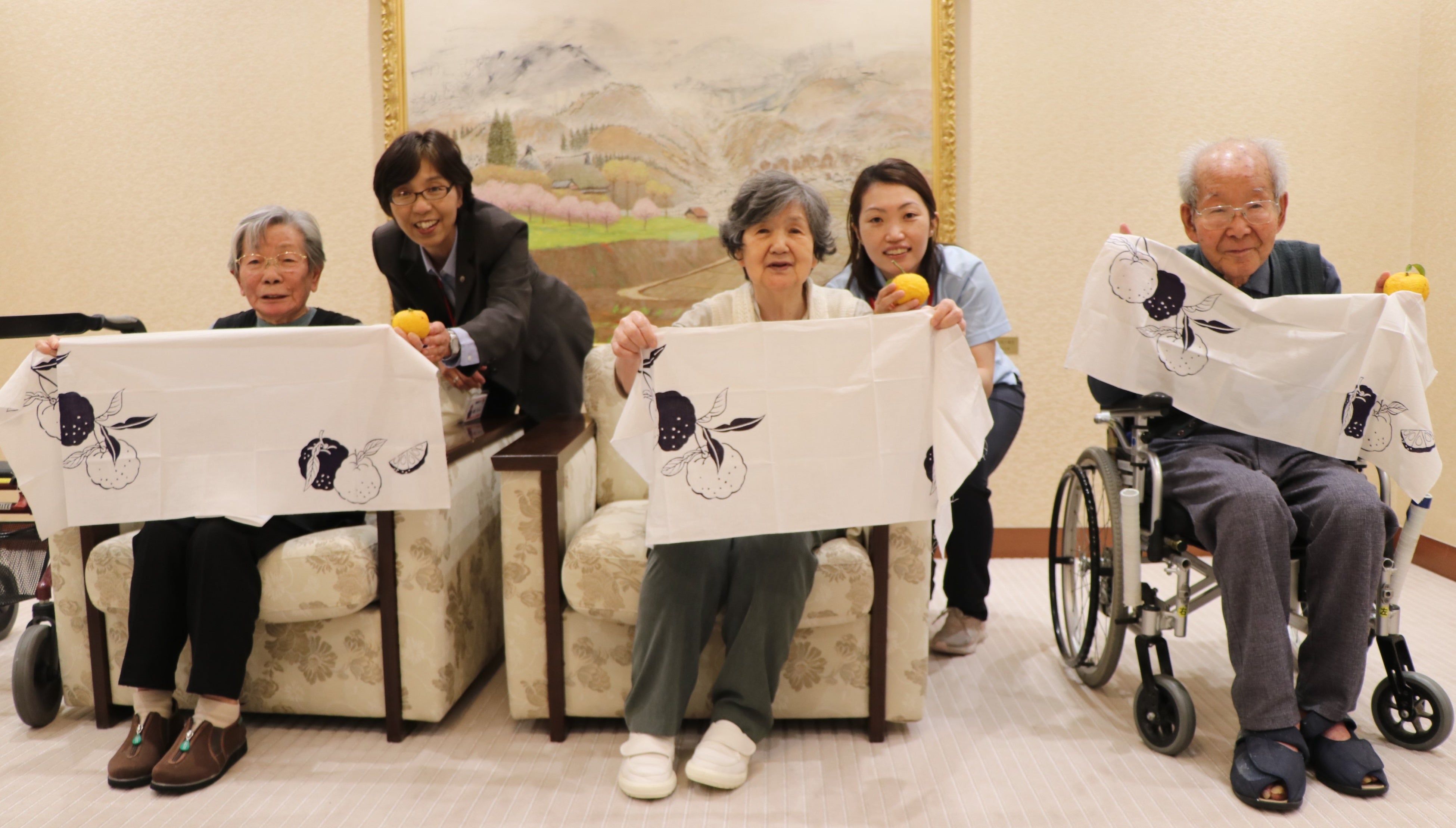 本物のユズと一緒に手拭いを広げ、笑顔を見せる皆さん 。「家族にもこの手拭いを見せたいですね」（阿木とよ子さん　91歳：写真中央） （日本赤十字社総合福祉センターレクロス広尾：東京都）