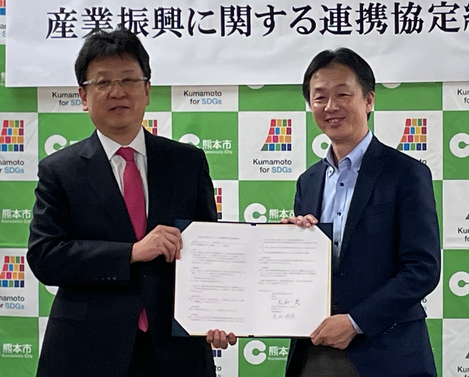 写真：大西一史・熊本市長(左)と協定書を取り交わす、荒井邦彦・当社代表取締役社長（右）