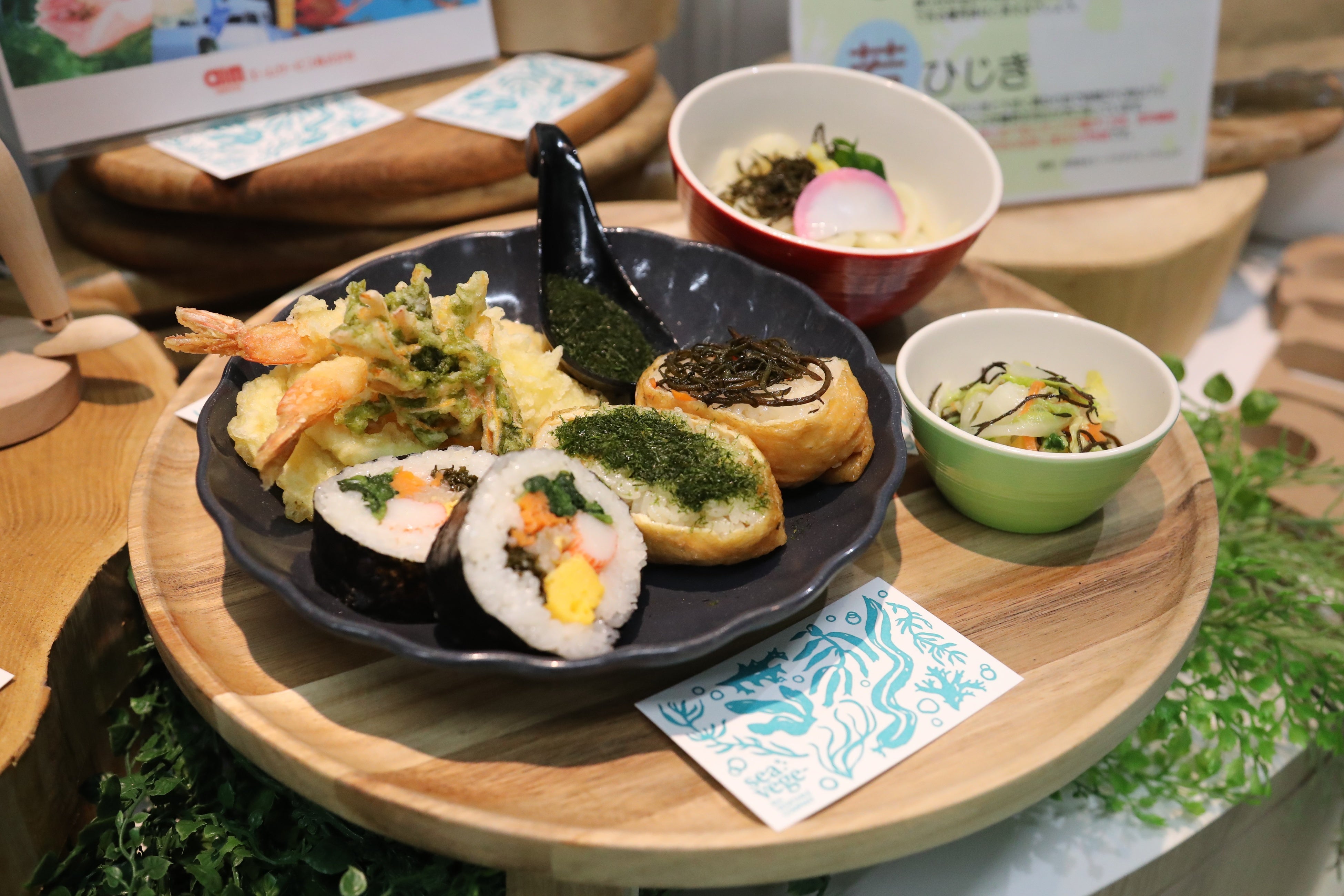 シーベジタブルの養殖海藻を用いた提供メニュー（若ひじきとすじ青のりの稲荷寿司、若ひじきのキンパ、天婦羅盛り合わせ（あつばあおさ天ほか）、若ひじき入り白菜の浅漬け、若ひじきミニうどん）
