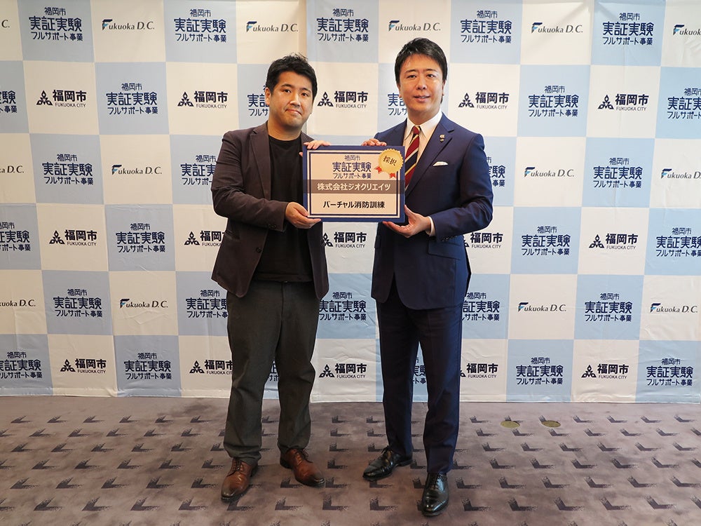 採択式の様子：(左)ジオクリエイツ代表取締役 本田 司／(右)福岡市 高島 宗一郎 市長