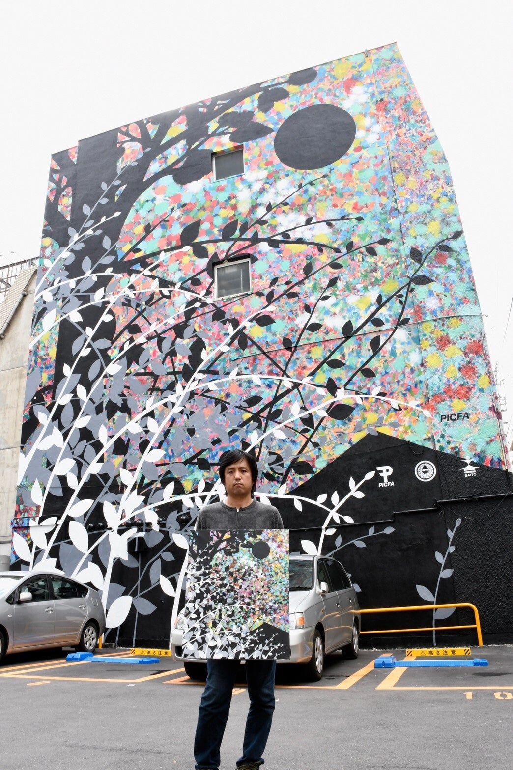 本田雅啓さんが手にしている作品《ホシゾラ》（2018年）を再現したウォールアート（福岡市博多区）