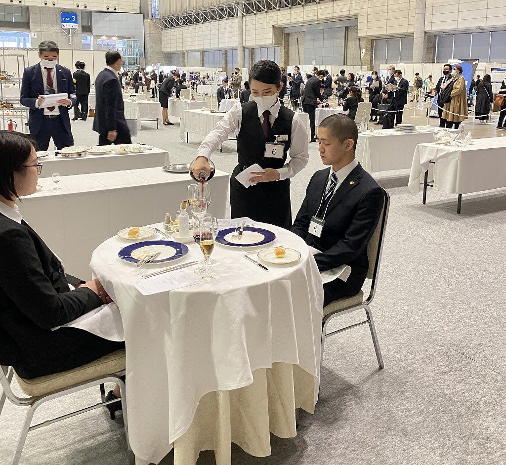 デキャンタからこぼさないように赤ワインのサービスをする蓬田さん（中央）