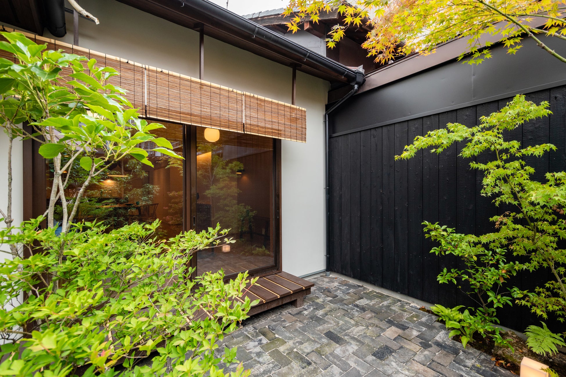 焼杉板塀、ヘリンボーン貼りの上海レンガ、杉+竹の縁側、そして簾が植栽と調和し、居心地のいい坪庭
