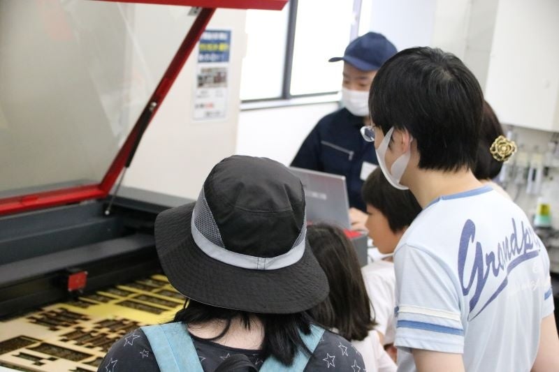 レーザー加工機を使って、パソコンで作成したデザインを切断している様子を眺める参加者