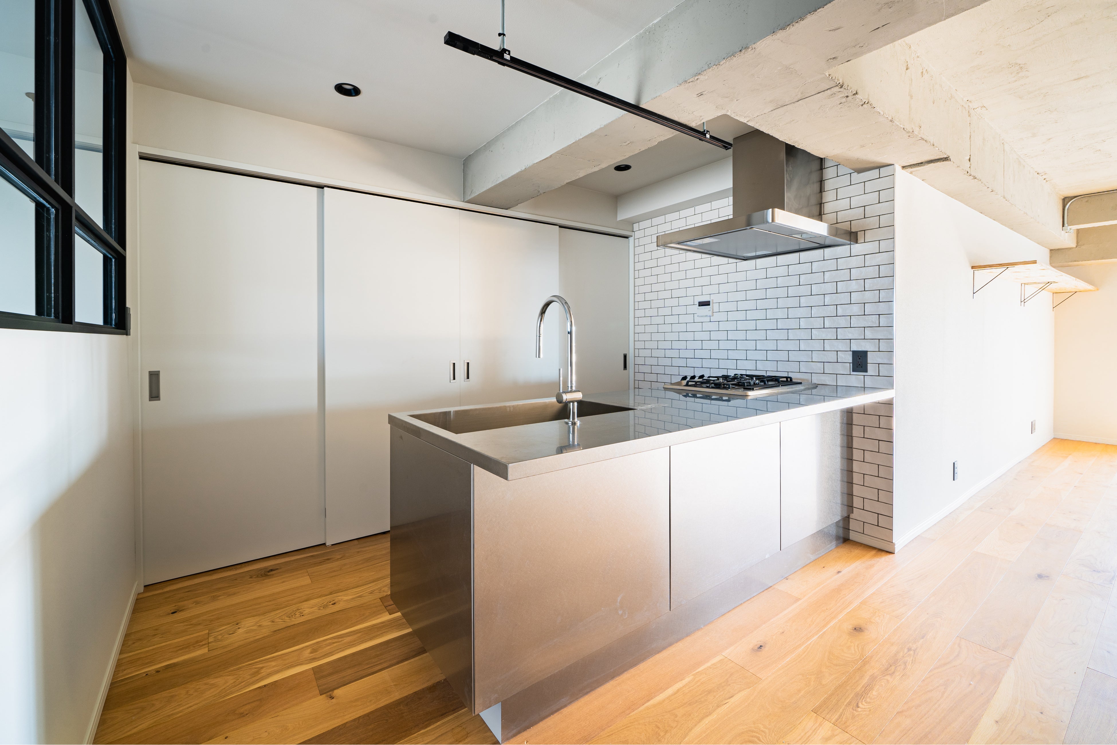 存在感のあるステンレスキッチン。壁面は白いタイル、天井はコンクリート現し