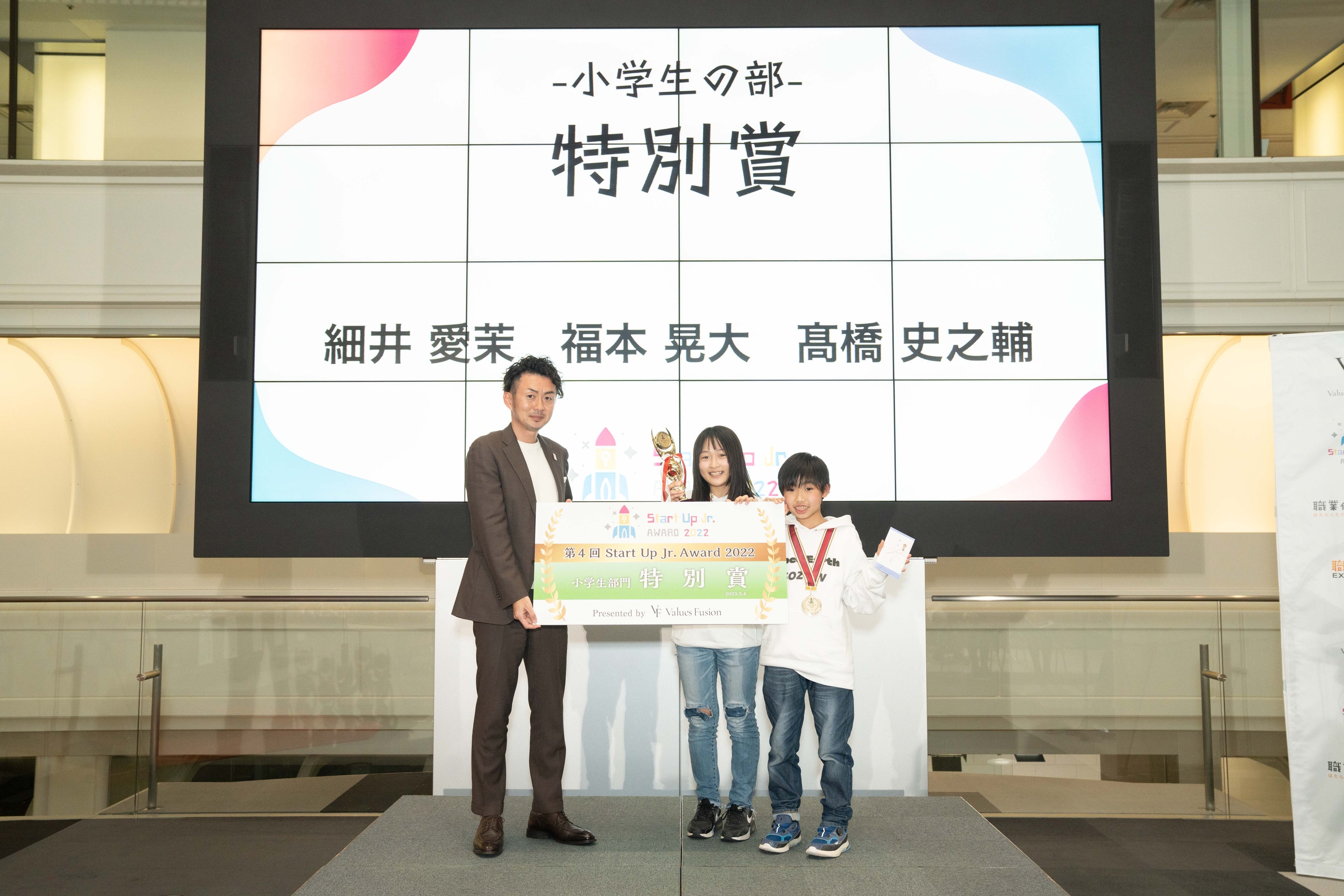 審査員の（公社）2025年日本国際博覧会協会 機運醸成局 岡田和正氏よりトロフィーとパネルを授与される細井愛茉さん、福本晃大さん