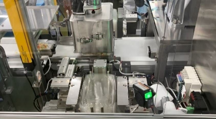 手前に積み上げた容器のふたをロボットアームが取り、惣菜の容器に押し付ける