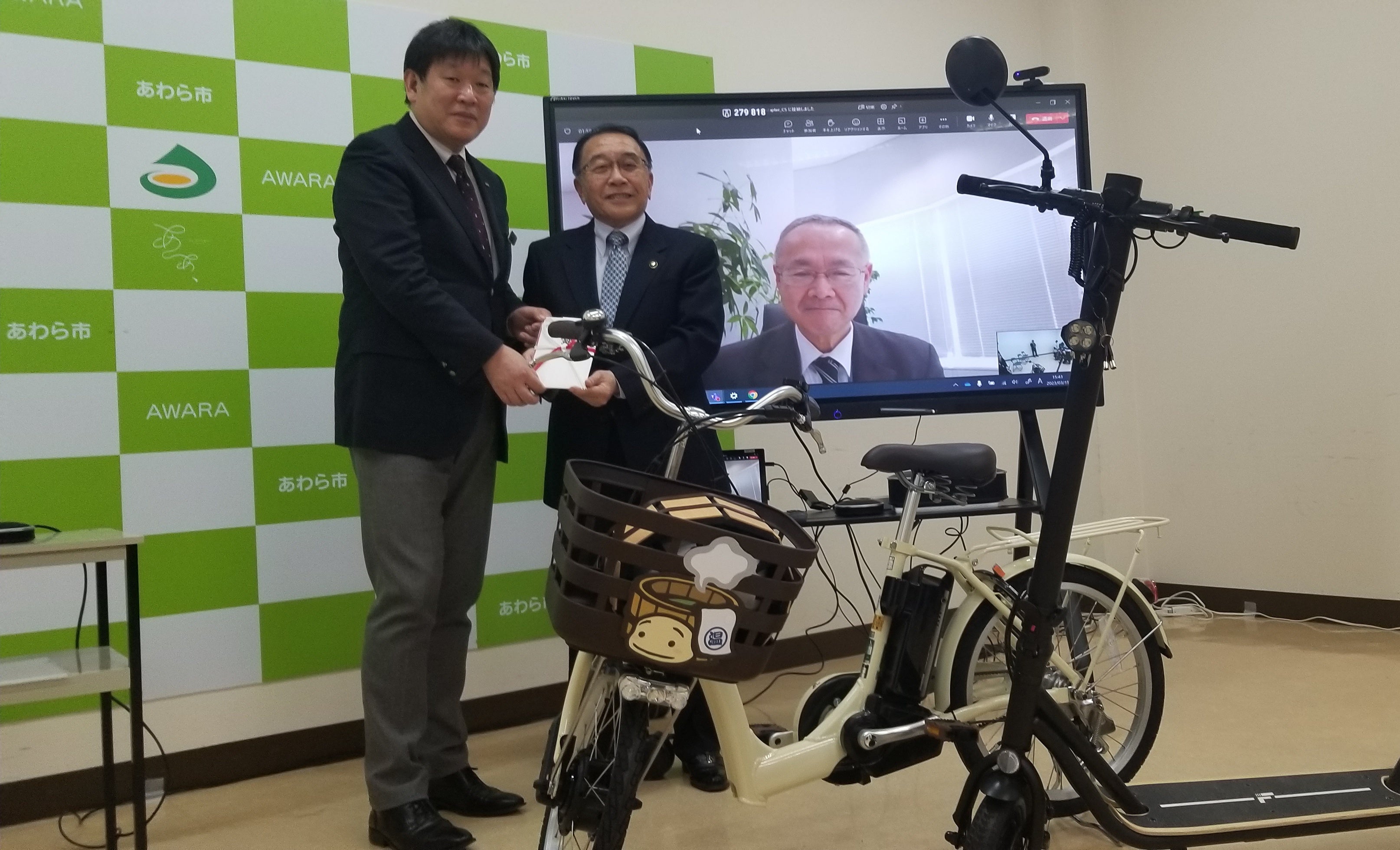 あわら市役所で行われた寄贈式にて　実際に運用される電動アシスト自転車および電動キックボードとともに　※左から、日本旅行・秋山取締役、あわら市・森市長、日本旅行・小谷野社長（オンライン参加）