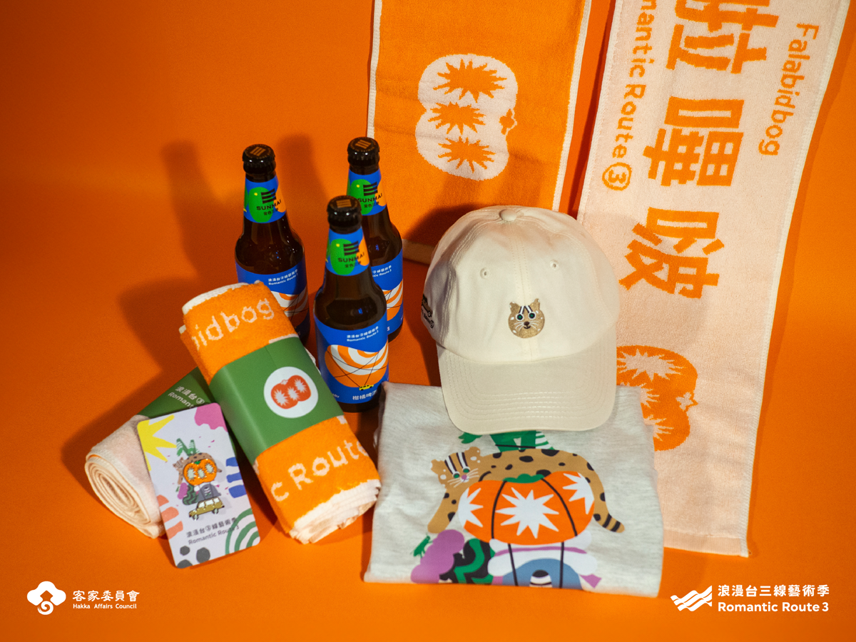 芸術祭限定グッズ：Tシャツ、タオル、ピンバッジ（車と柿の2種）、帽子、オレンジビールなど。©️ロマンチック台三線芸術祭