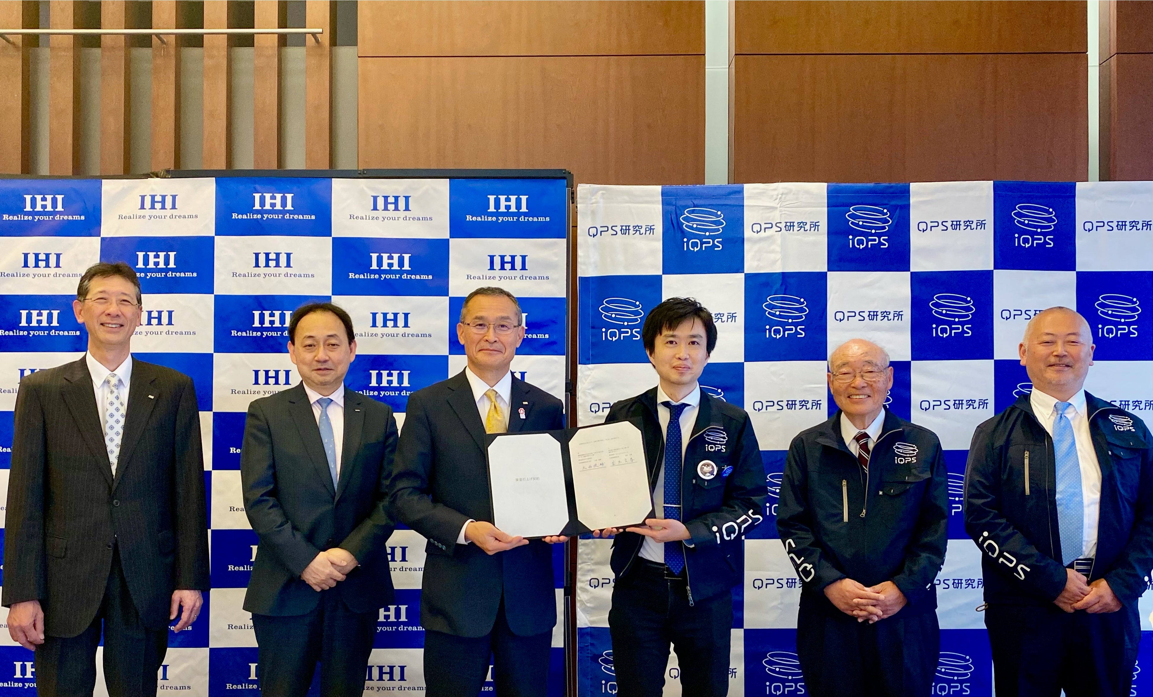 締結式の記念写真。左から、IA石川智孝取締役、IA永山隆司取締役、IA並木文春代表取締役社長、QPS研究所代表取締役社長CEO 大西俊輔、QPS研究所創業者・取締役・九州大学名誉教授 八坂哲雄、QPS研究所取締役 松本崇良。