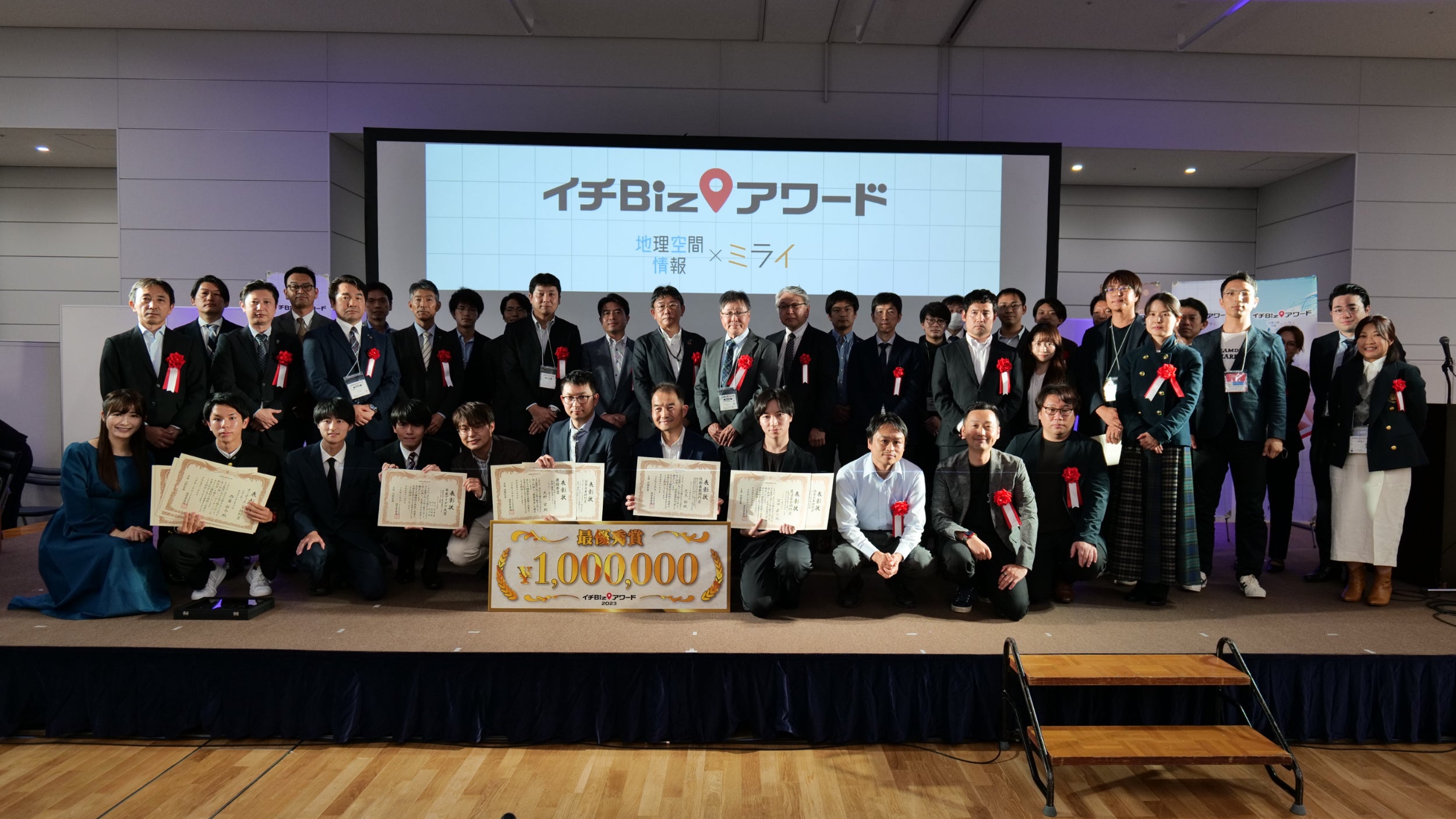 表彰式のステージにて賞状を手に笑顔の受賞者と審査員ら